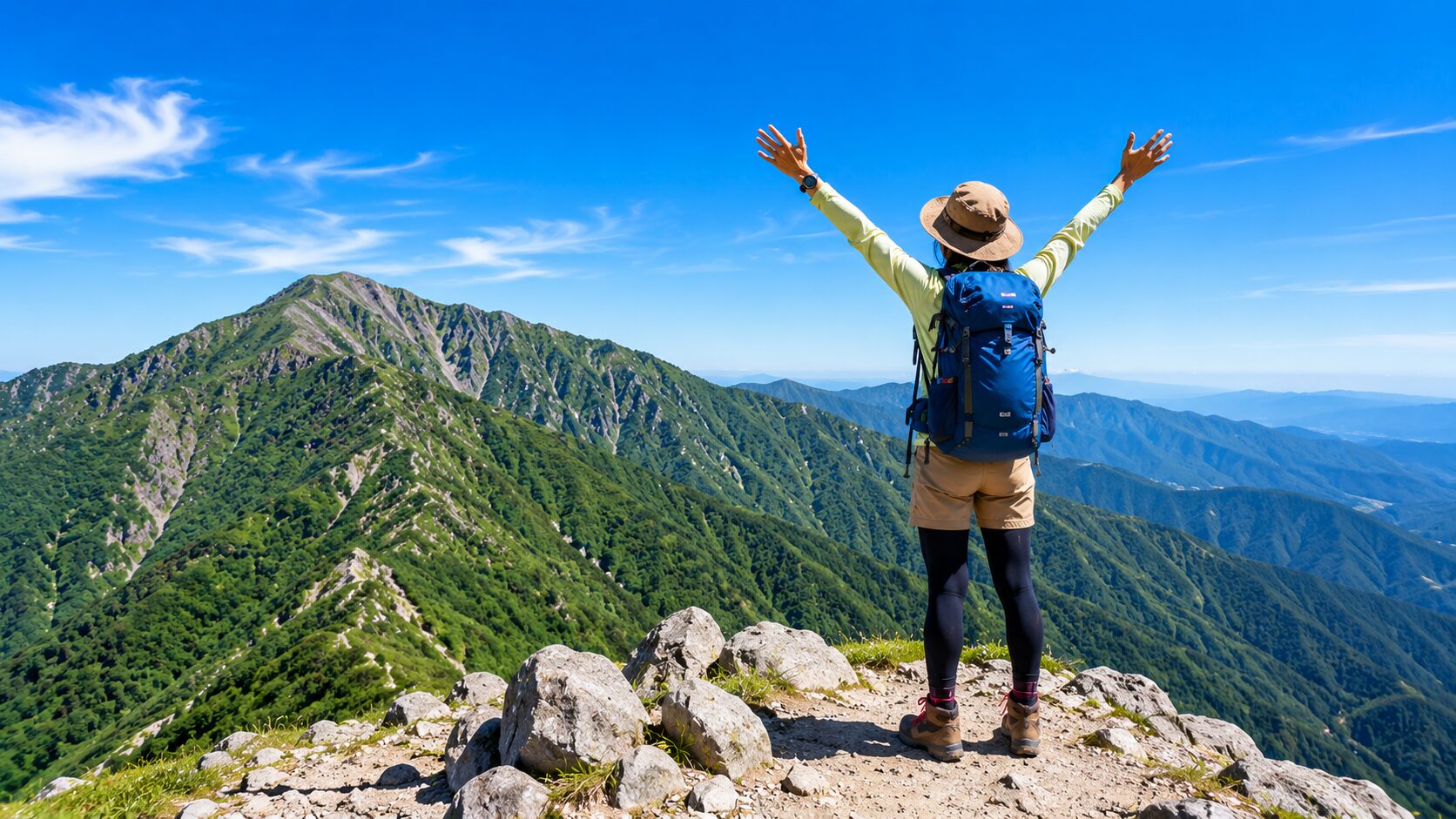 青空の山頂で両手を広げる登山者