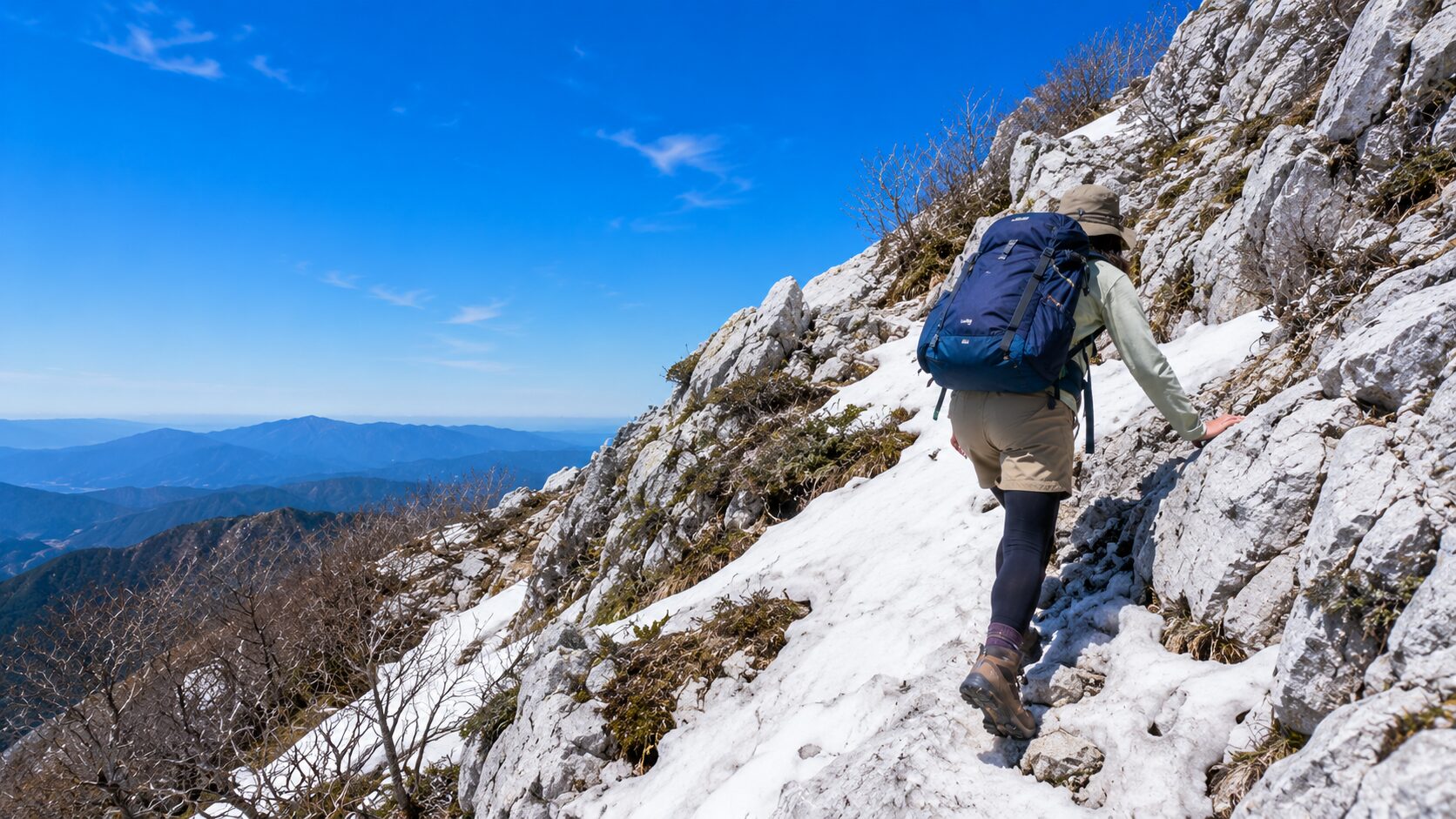 藤原岳の残雪が残る春山の岩場を登る登山者